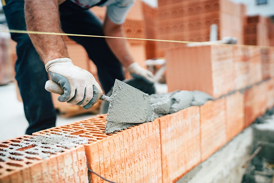 Masonry Contractor Insurance - Professional Masonry Worker Using Pan Knife for Building Brick Walls with Cement and Mortar