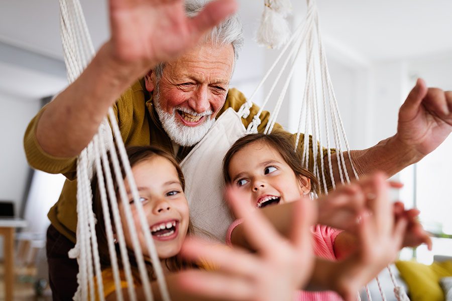 Client Center - Closeup View of a Cheerful Grandfather Playing with His Granddaughters as They Sit in a Hammock at Home