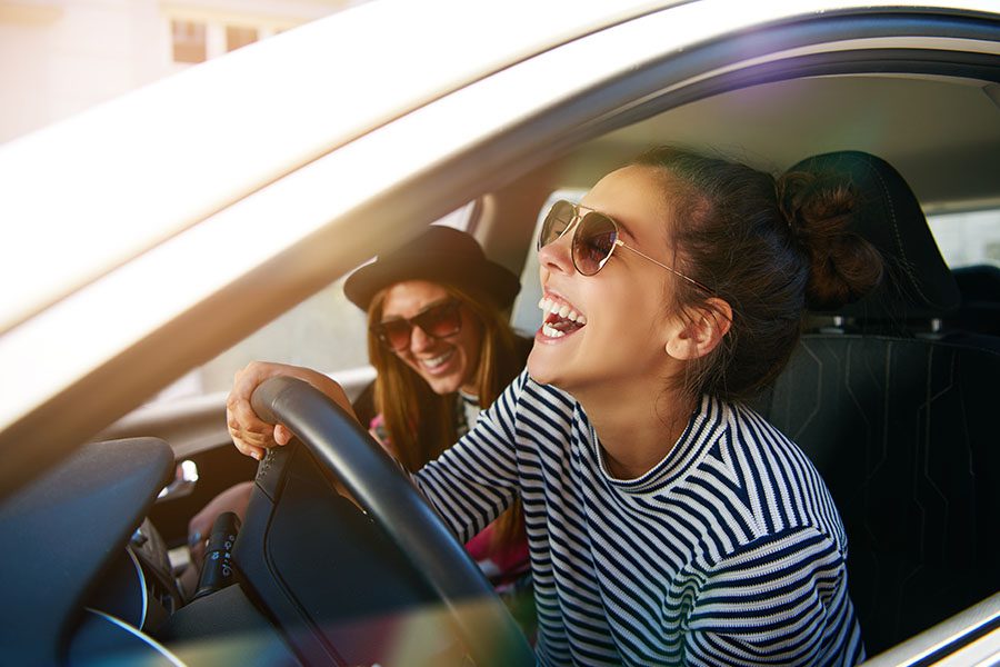 Contact - Closeup View of Cheerful Woman Wearing Sunglasses Driving a Car and Having Fun with Her Friend in the Passenger Seat